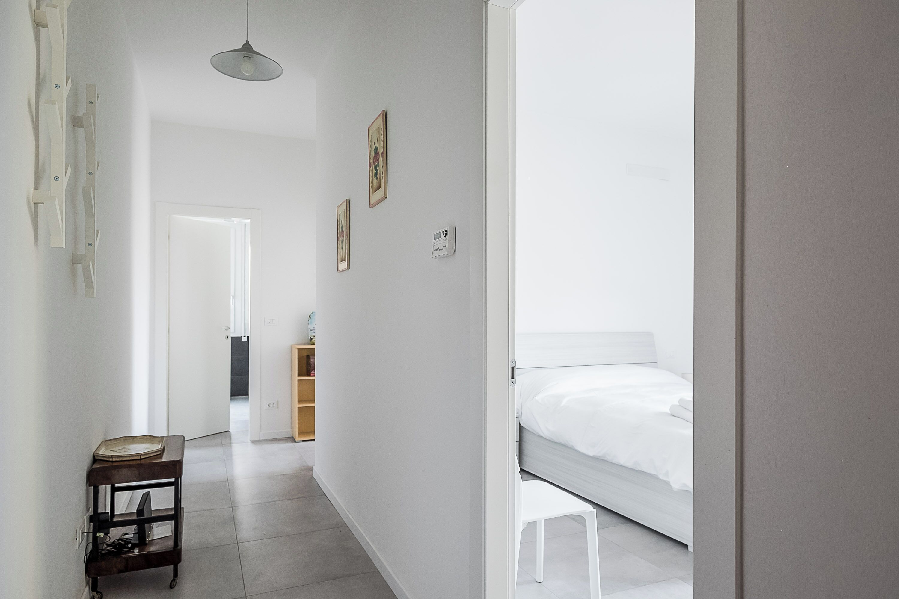 A modern, minimalist bedroom with a single bed, a small table, and a hanging light fixture.