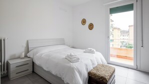 A bedroom with a bed, a nightstand, a window with a view, and two wall decorations. - Appartamento Bernini in zona Sant'Orsola by Wonderful Italy (Bologna)