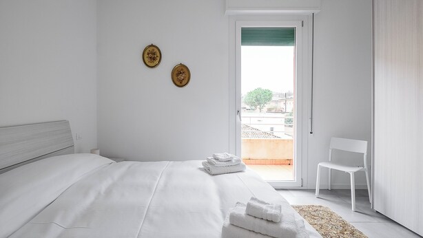 A modern bedroom with a large bed, a chair, and a view of the outside. - Appartamento Bernini in zona Sant'Orsola by Wonderful Italy (Bologna)