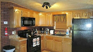 A kitchen with wooden cabinets, a black stove, a microwave, and a refrigerator.