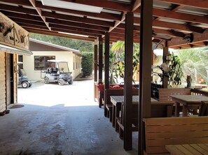 A covered outdoor seating area with wooden tables and benches, a golf cart, and a building in the background.