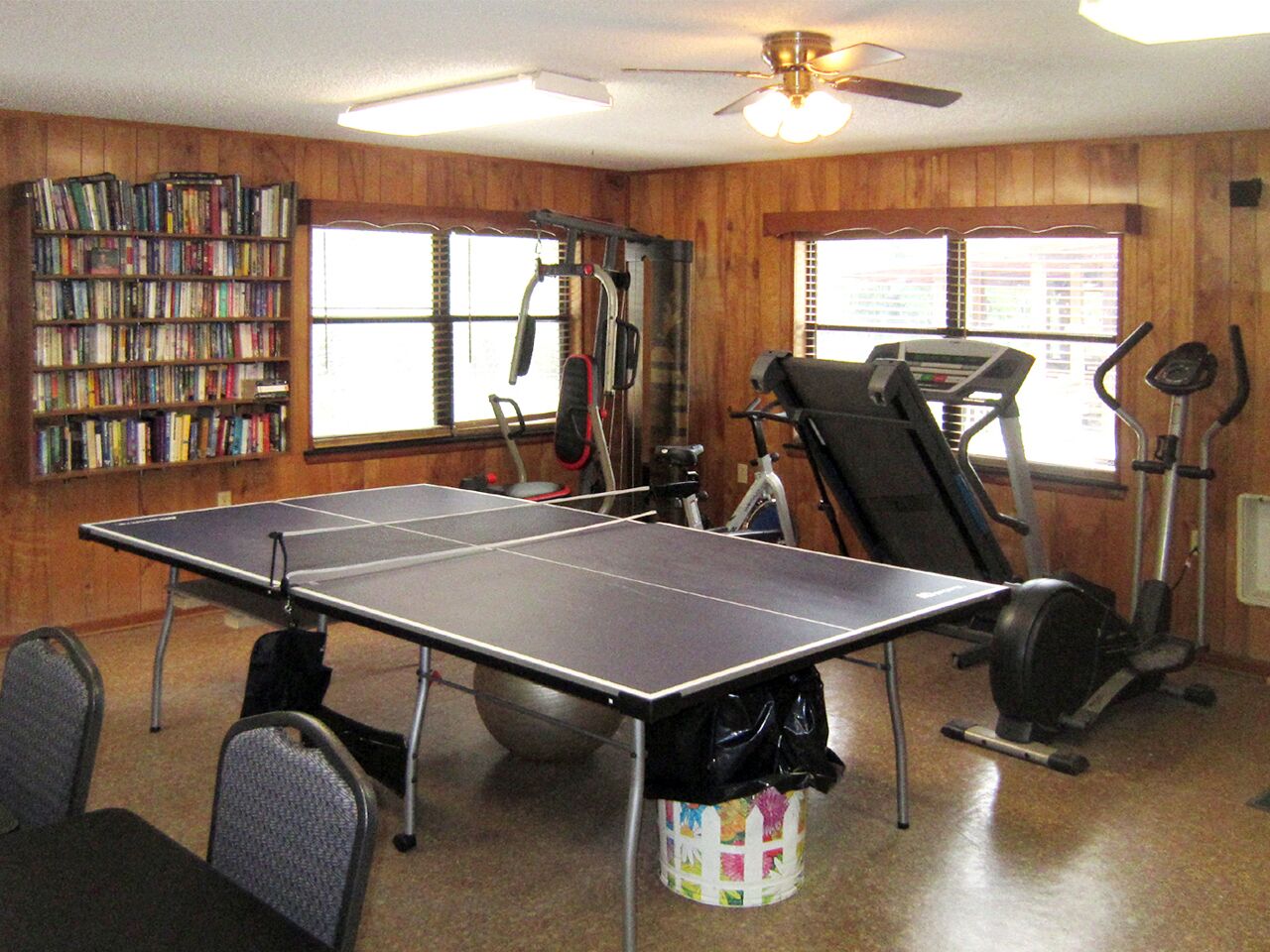 Une pièce équipée d’une table de ping-pong, de matériel d’exercice et d’une bibliothèque.