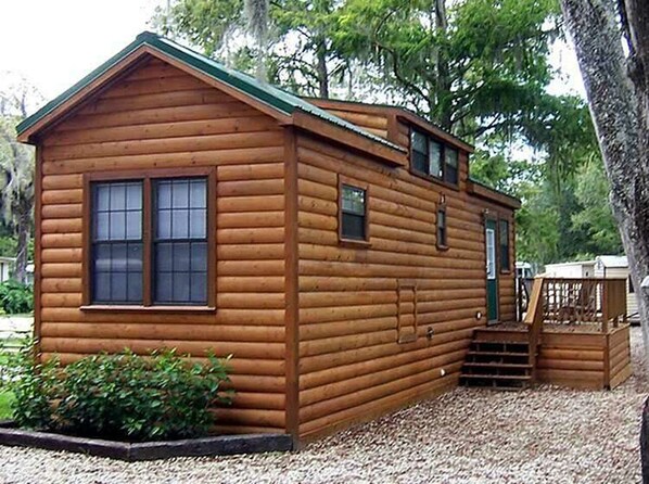 Une petite cabane en bois avec un toit vert, une porte d’entrée et un petit porche.