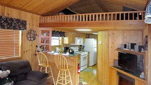 A cozy cabin interior with a dining area, kitchen, and a TV in the living room. - Cozy Cabin in riverfront resort (Inverness)