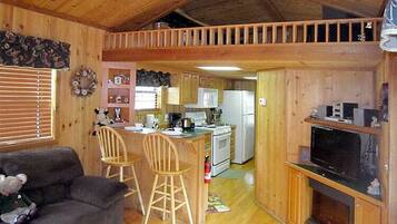 A cozy cabin interior with a dining area, kitchen, and a TV in the living room.