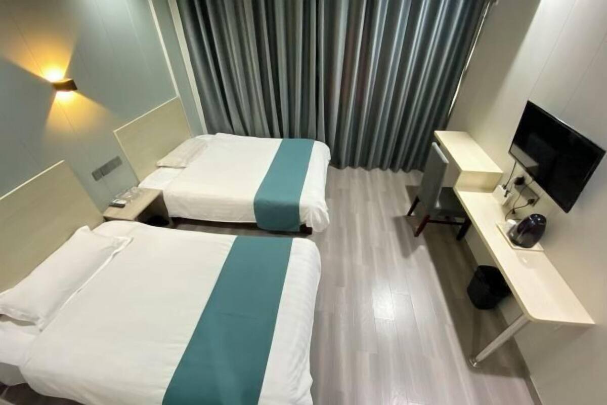A hotel room with two beds, a desk, a television, and a curtain.