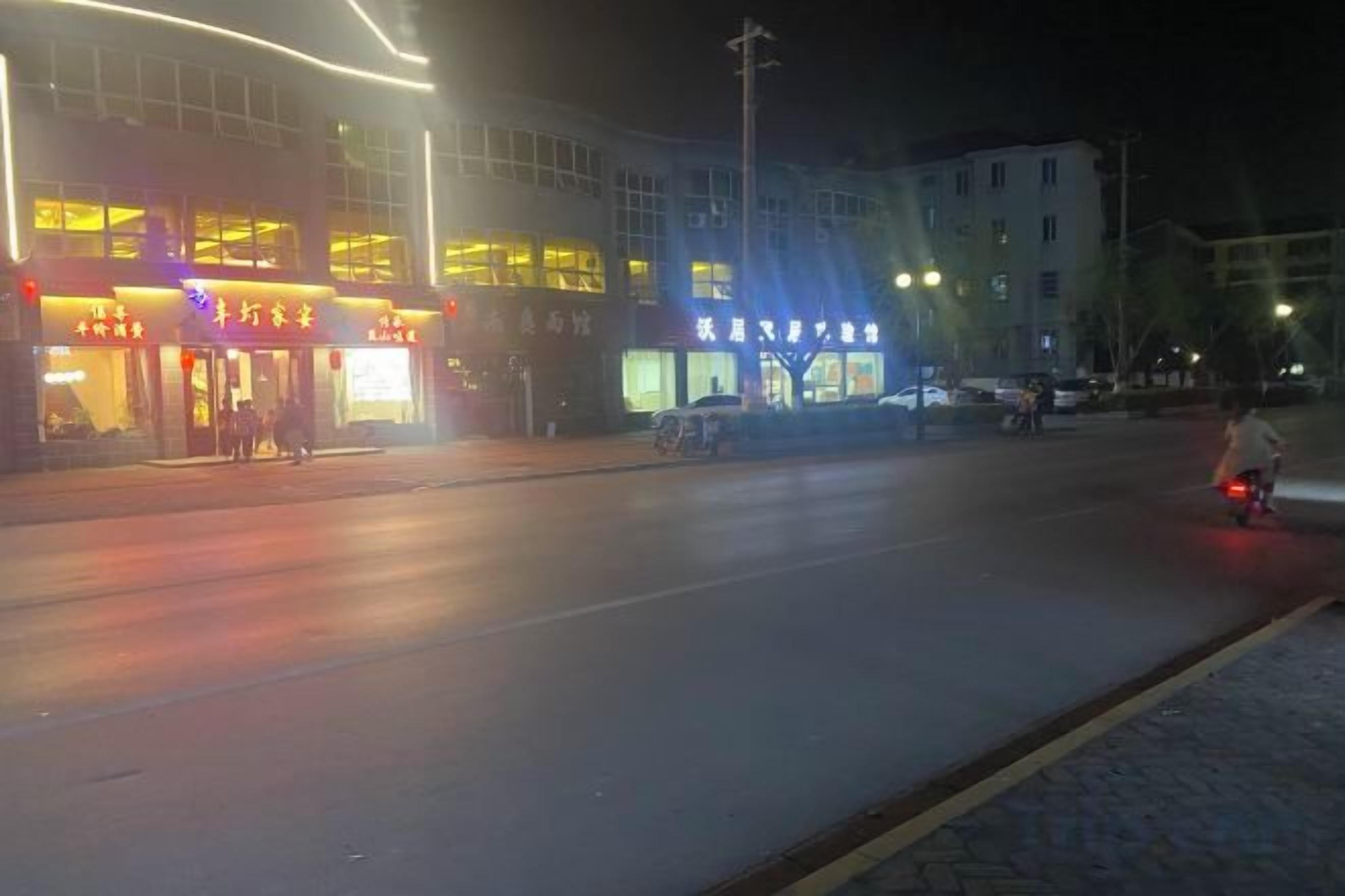 A street at night with illuminated storefronts and a clear road.