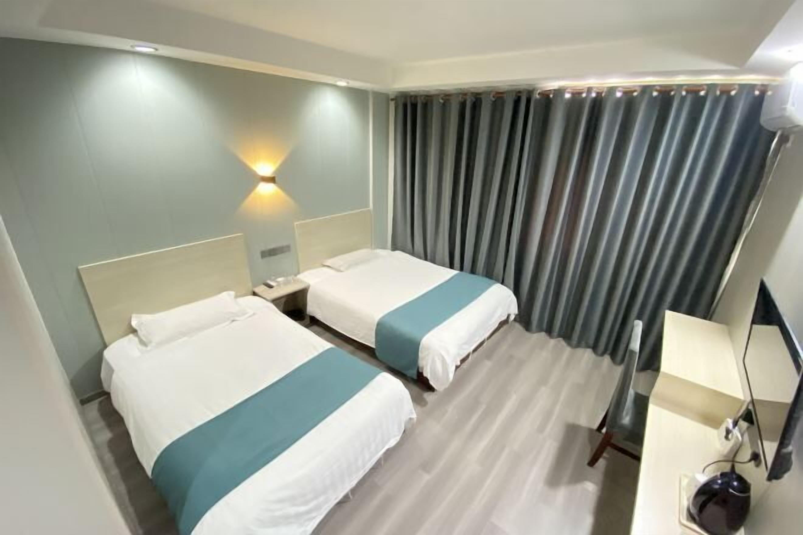 Ein Hotelzimmer mit zwei Betten, einem Nachttisch, einem Schreibtisch mit Lampe und einem Fenster mit Vorhängen.