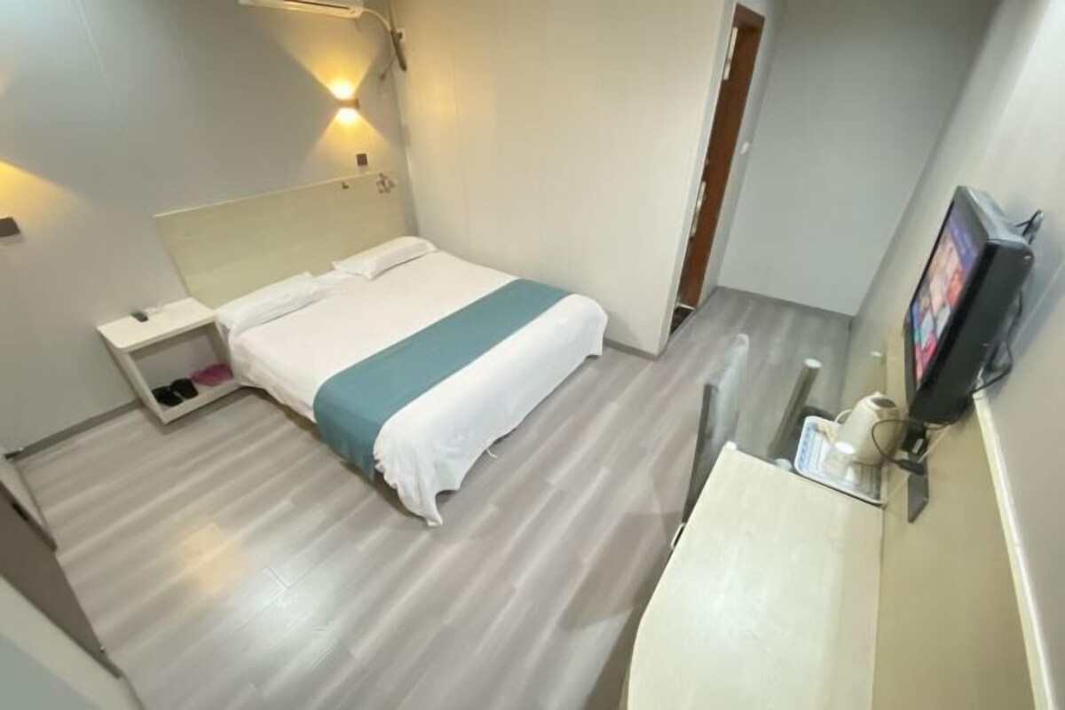 Habitación de hotel con cama, mesita de noche y televisión montada en la pared.