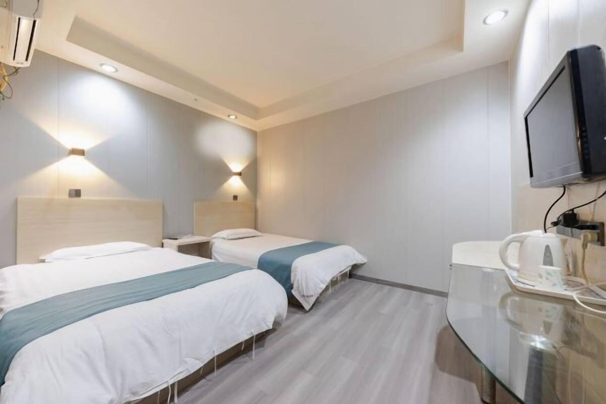 A hotel room with two beds, a flat-screen TV, a coffee maker, and a glass table.