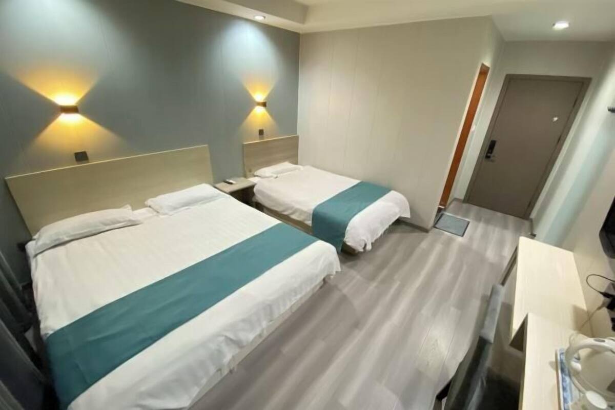 A hotel room with two beds, a desk, a chair, and a door.