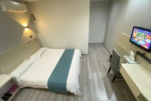 Habitación de hotel con cama, escritorio, silla, televisor y aire acondicionado de pared.