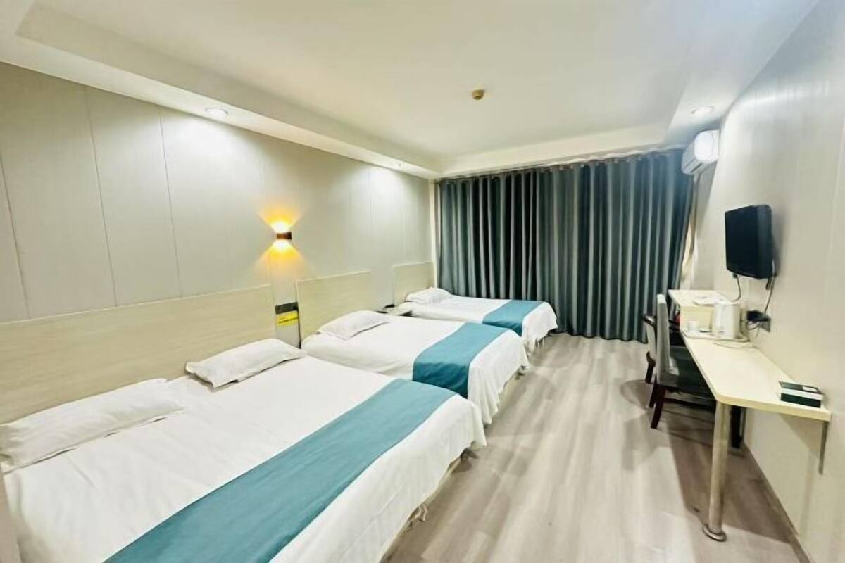 A hotel room with two beds, a desk, a chair, a lamp, and a curtain.
