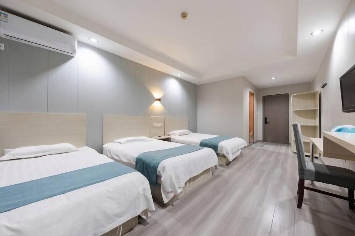 A hotel room with three beds, a desk, a chair, a TV, and an air conditioning unit.