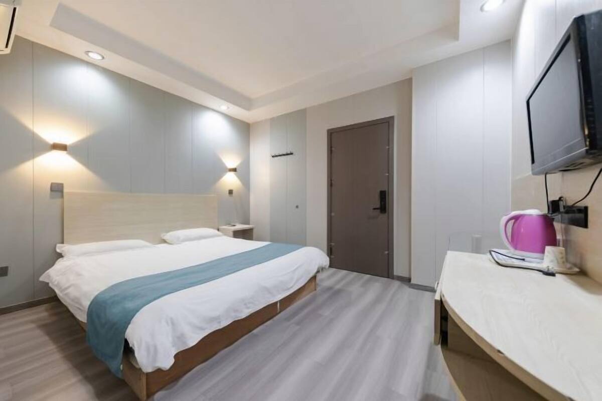 A hotel room with a bed, bedside tables, a TV, and a door.