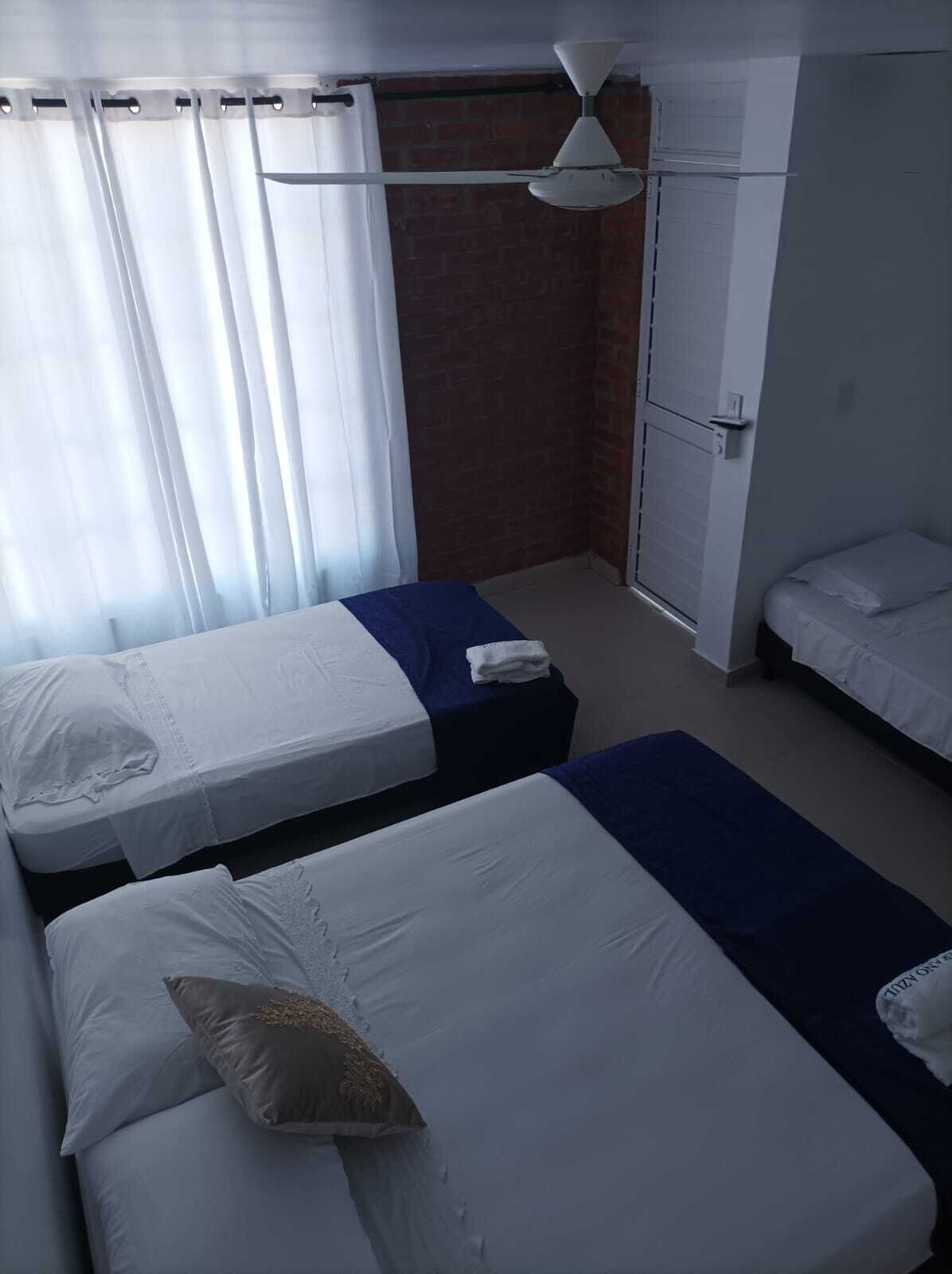 A hotel room with two single beds, a ceiling fan, a brick wall, and a window with curtains.