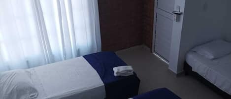 A hotel room with two single beds, a ceiling fan, a brick wall, and a window with curtains.
