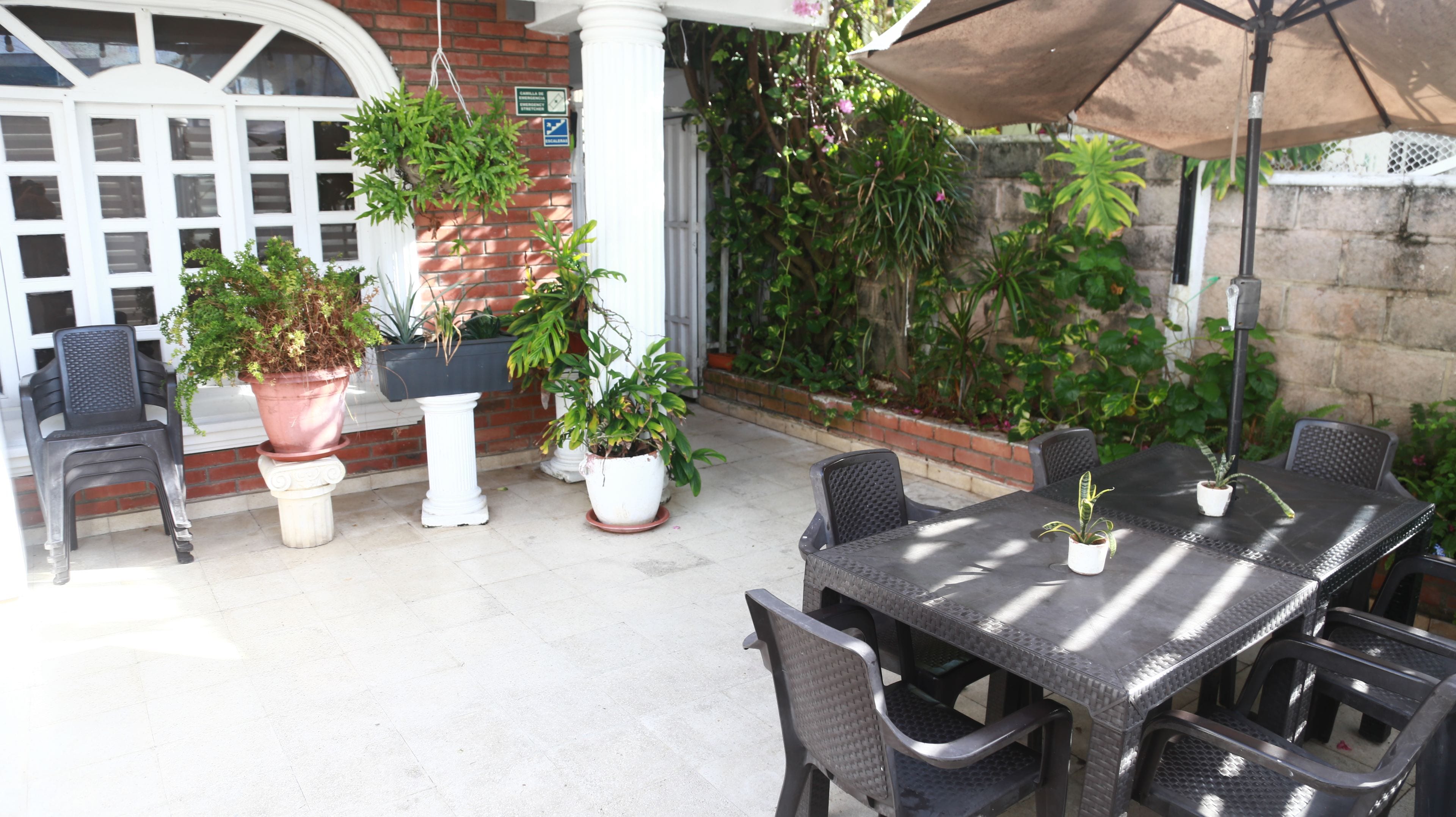 Een terras buiten met een tafel, stoelen, potplanten en een bakstenen muur.