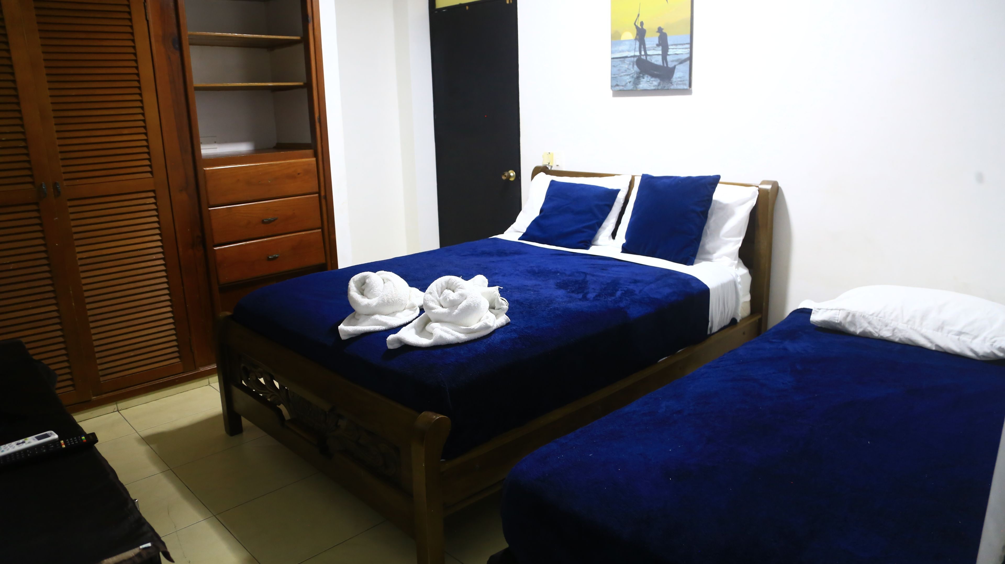 A bedroom with two beds, a wardrobe, and a painting on the wall.