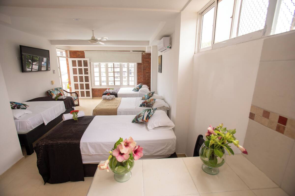 Quarto de hotel com duas camas de solteiro, um sofá, uma mesa de jantar e um ventilador de teto.