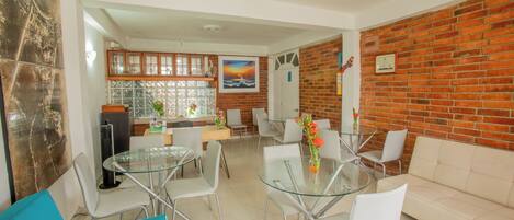 A modern living room with a glass dining table, white chairs, a beige sofa, and a brick wall.