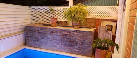 A swimming pool with a stone wall and potted plants.
