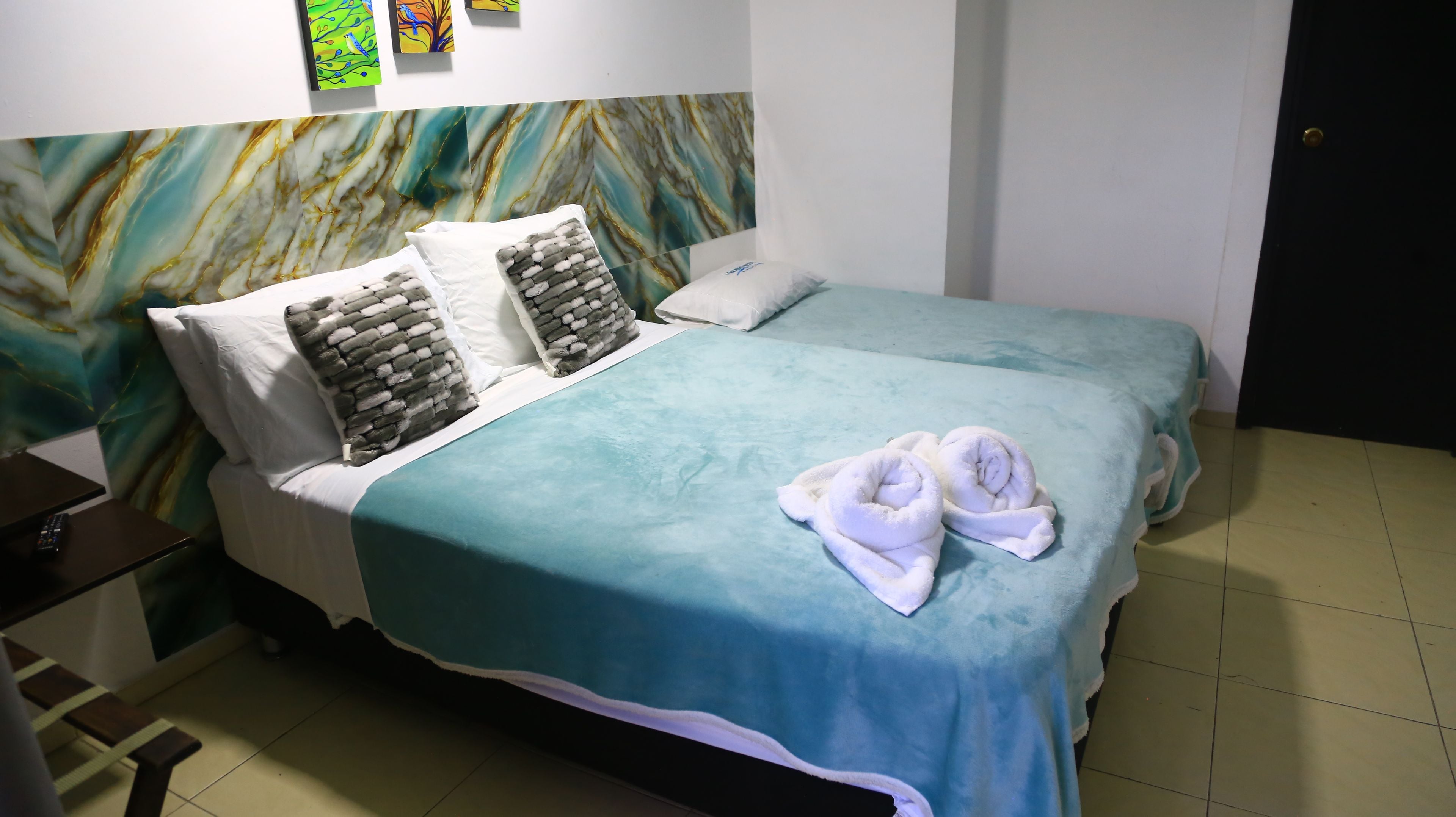 Une chambre d’hôtel avec deux lits, une table de chevet et un mur orné d’un motif évoquant le marbre.