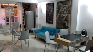 A modern living room with a blue sofa, a glass dining table, and a white chair. There is a refrigerator, a clock, and a framed map on the wall. - HOTEL VERANO AZUL (San Andrés)
