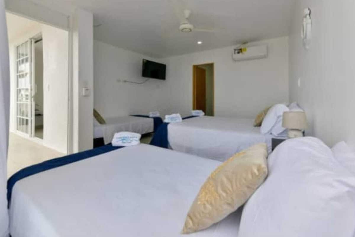 Quarto de hotel com duas camas, uma televisão na parede e porta que dá para uma varanda.