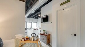 Una habitación de hotel moderna con kitchenette, una cama con cubrecama acolchado, una mesita de madera con hervidor y un cartel que indica la ubicación como Nashville, TN.