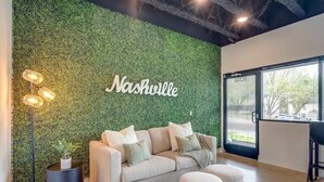 Una sala de estar moderna con una pared verde, un sofá, otomanas y una lámpara de pie.
