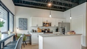 Una cocina moderna con armarios blancos, una isla central, electrodomésticos de acero inoxidable e iluminación colgante.
