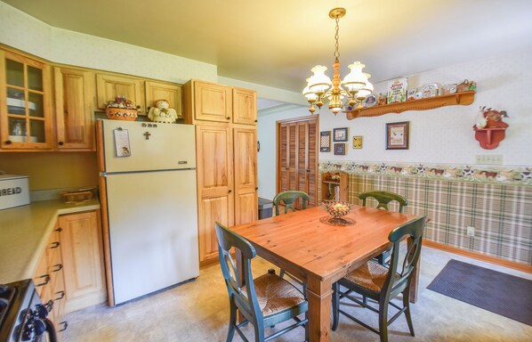 A kitchen with wooden cabinets, a refrigerator, a dining table with chairs, and a chandelier.