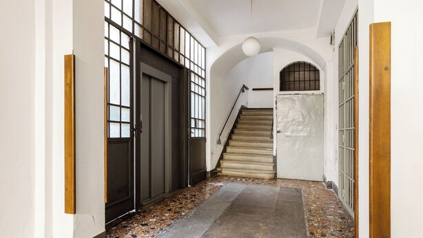 A hallway with a tiled floor, a staircase, and a door with barred windows. - White Leaves Studio by Wonderful Italy (Bologna)