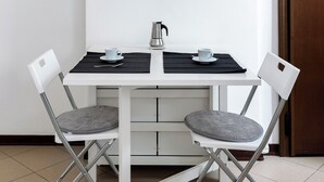 A compact dining area with a white table, two chairs, a small coffee pot, and a decorative wall piece. - White Leaves Studio by Wonderful Italy (Bologna)