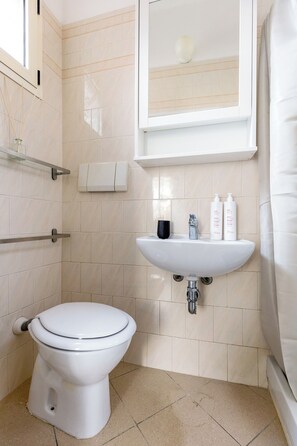 A bathroom with a white toilet, a sink with toiletries, and a mirror above the sink.