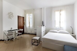 A room with a bed, a desk with chairs, a small stool, and a wardrobe.