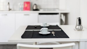 A modern kitchen with white cabinets, a coffee maker, and a dining table set with a black placemat, a cup, and a spoon. - White Leaves Studio by Wonderful Italy (Bologna)