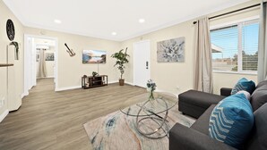 Un salon spacieux doté d’un parquet, d’un canapé gris agrémenté de coussins bleus, d’une table basse en verre et d’un tableau accroché au mur.
