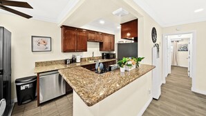 Une cuisine moderne dotée de plans de travail en granit, d’appareils électroménagers en acier inoxydable et d’armoires en bois.