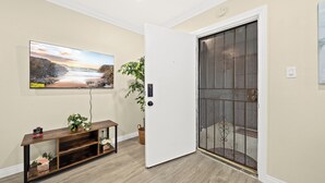 Une pièce avec une console en bois, une plante en pot, une porte surmontée d’une grille en métal et un tableau encadré accroché au mur.