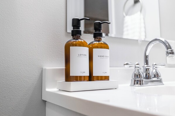 A bathroom sink with two bottles of lotion and hand soap on a white soap dish.