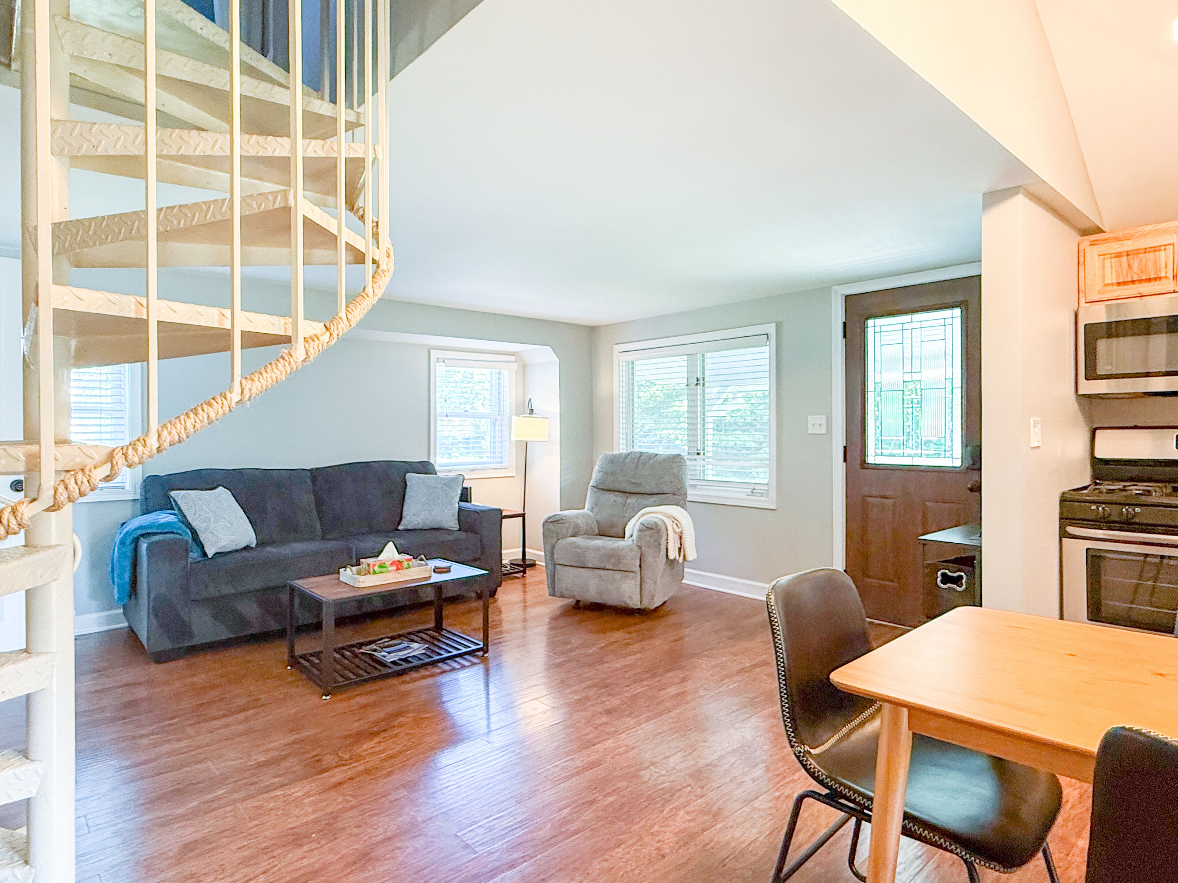 A spacious living area with a wooden staircase, a sofa, a coffee table, and a dining table with chairs.