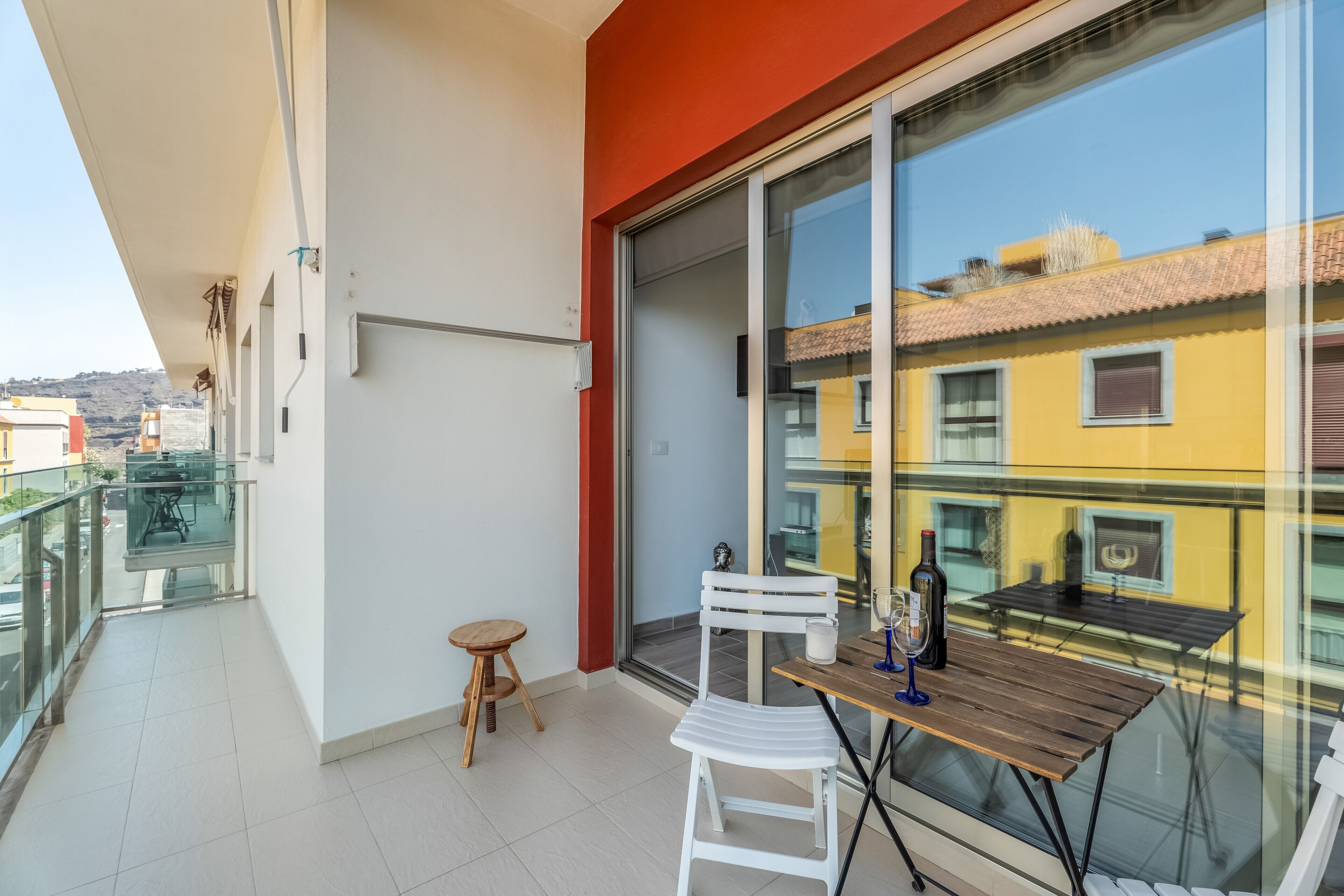 Un balcon avec une table en verre, une chaise blanche et un petit tabouret.