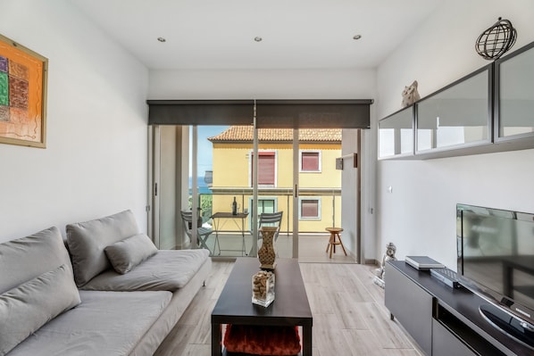 Un salon moderne comprenant un canapé, une table basse, un téléviseur et un balcon avec une table et des chaises.