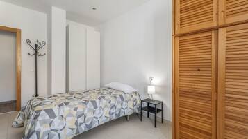 A bedroom with a bed, a nightstand with a lamp, a coat rack, and a wooden wardrobe.