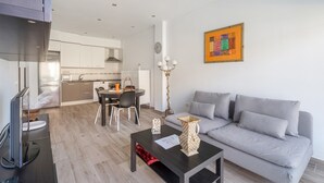 A modern living room with a grey sofa, a coffee table, and a TV. There is a dining area with a table and chairs, and a kitchen in the background. - 'Casa Graham' Apartment with Sea View, Balcony and Wi-Fi (Tazacorte)