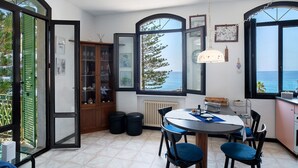A dining area with a table and chairs, a view of the sea, and a cabinet with glass doors.