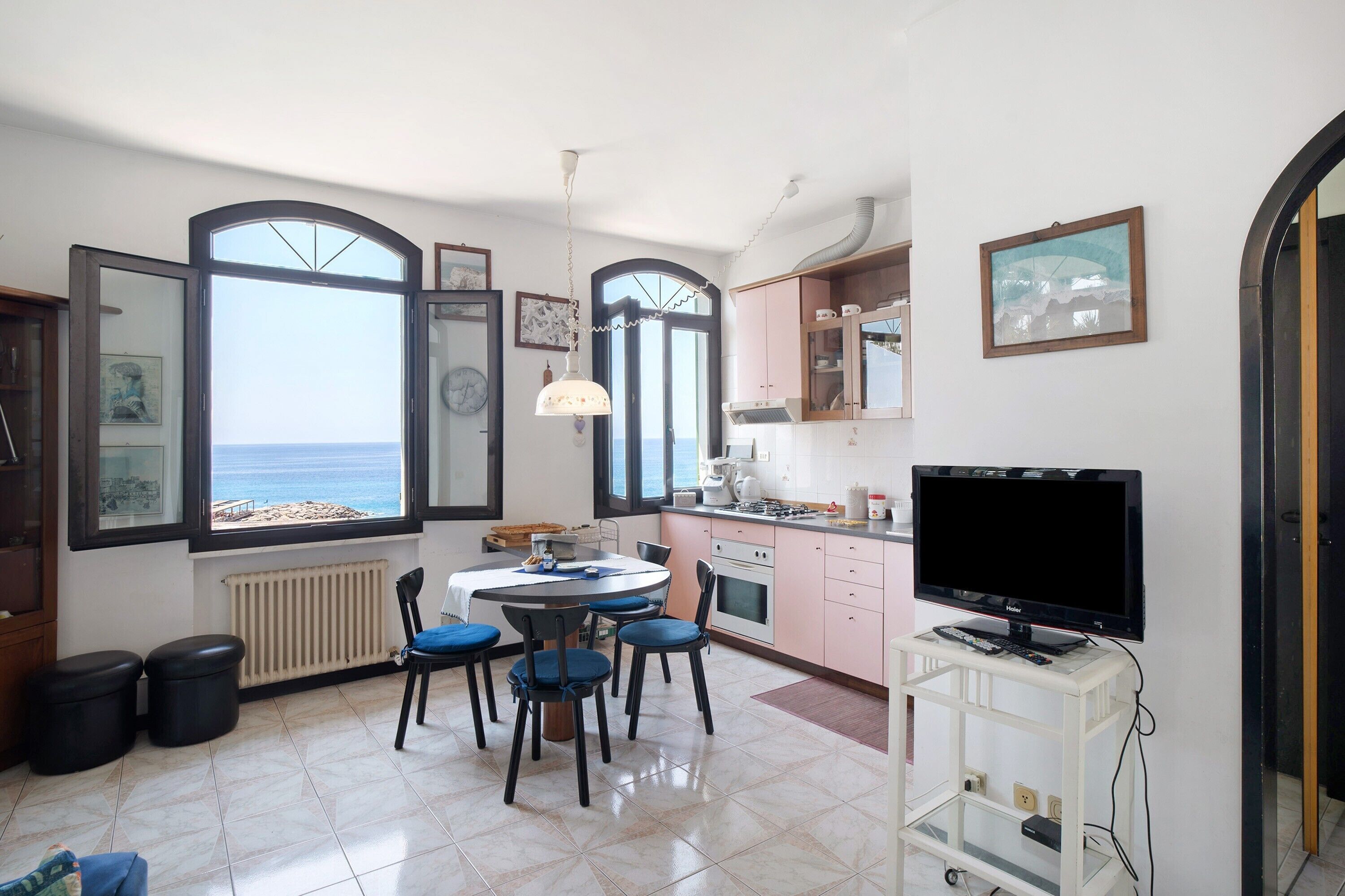 A modern kitchen with a dining area, large windows, and a TV.