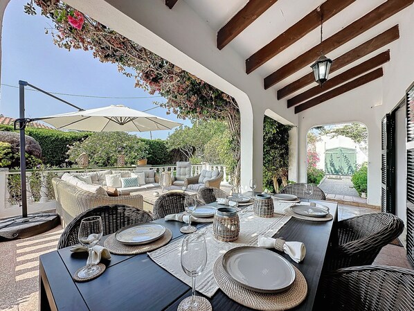 An outdoor dining area with wicker furniture, round tables, and a pergola with climbing plants.
